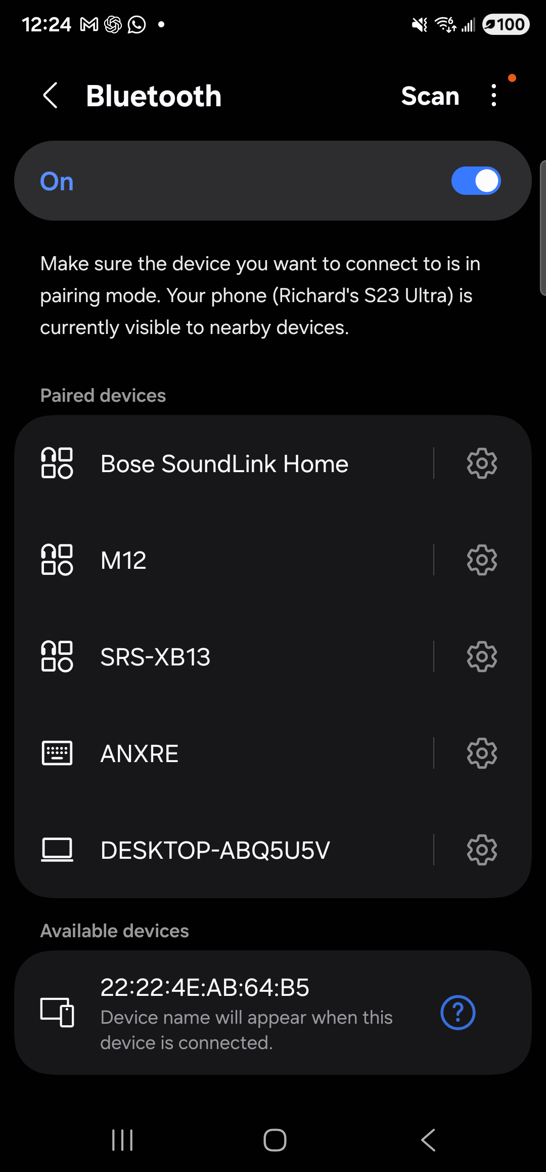 The Samsung Bluetooth settings page open full-screen on the Galaxy S23 Ultra in dark mode. The header at the top shows a back arrow, the title ‘Bluetooth’, a ‘Scan’ link and a three-dot overflow menu on the right. A pill-shaped row immediately below the header reads ‘On’ on the left with a switch toggled on, on the right. Beneath it, a short note: ‘Make sure the device you want to connect to is in pairing mode. Your phone (Richard’s S23 Ultra) is currently visible to nearby devices.’. A ‘Paired devices’ section then lists five entries — Bose SoundLink Home, M12, SRS-XB13, ANXRE, DESKTOP-ABQ5U5V — each with a small icon on the left and a settings cog on the right. Below them an ‘Available devices’ section shows a single nearby device by MAC address ‘22:22:4E:AB:64:B5’ with a question-mark icon on the right.