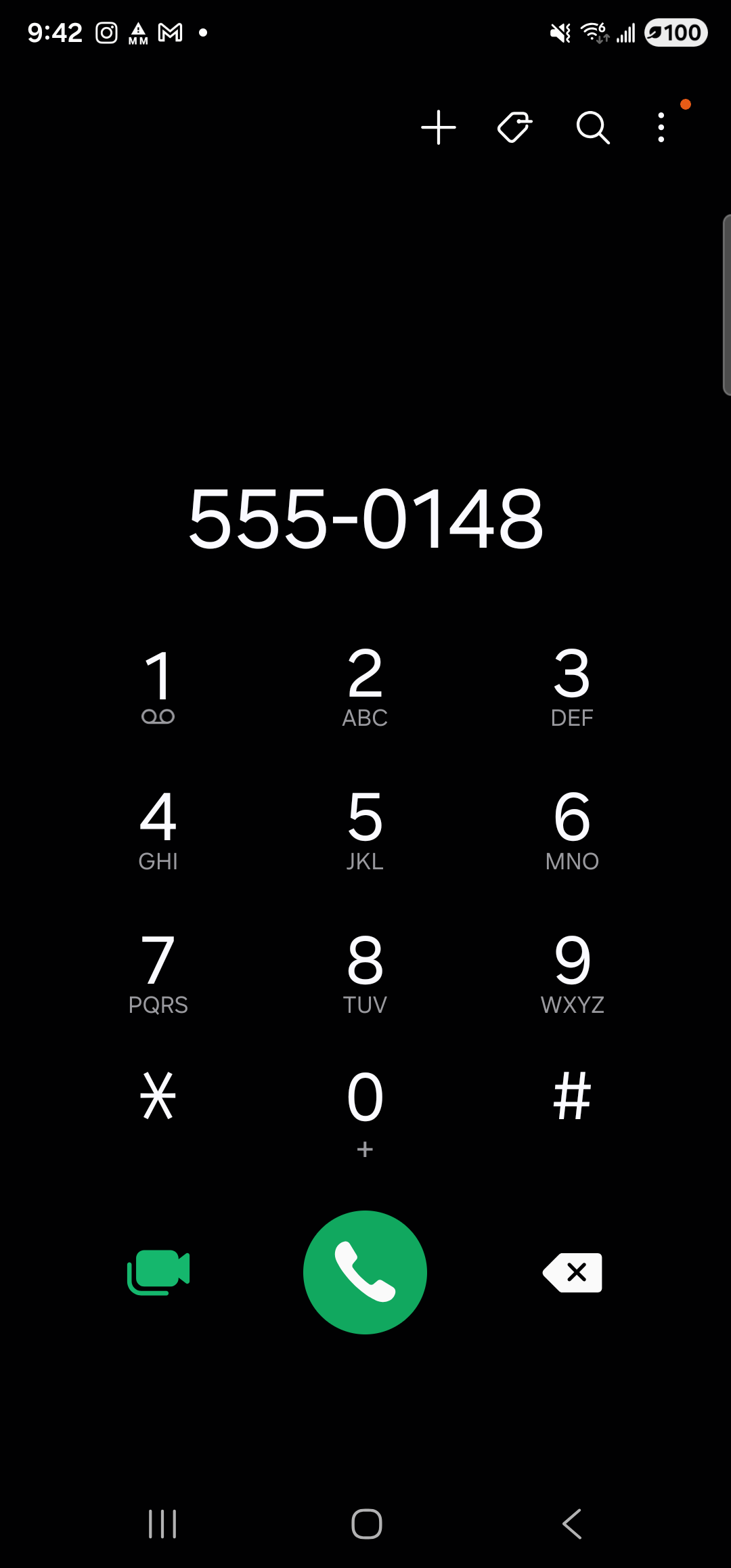 The Samsung Phone dialer full-screen on the Galaxy S23 Ultra in dark mode (black background, white digits). The status bar at the top shows the time 9:42 and a 100% battery indicator. A row of small header icons sits below: add-contact (+), tag, search, and an overflow menu (⋮). Centered near the top in very large white type are the digits ‘555-0148’ — the number Aside pre-filled. Below that, a full 12-key dialpad fills the middle of the screen with letters under each digit (1, 2 ABC, 3 DEF, 4 GHI, 5 JKL, 6 MNO, 7 PQRS, 8 TUV, 9 WXYZ, ✱, 0 +, #). At the bottom of the screen, a large round green button with a white phone icon sits centered, with a green video-call icon to its left and a white backspace ✕ icon to its right. The call has not been placed.