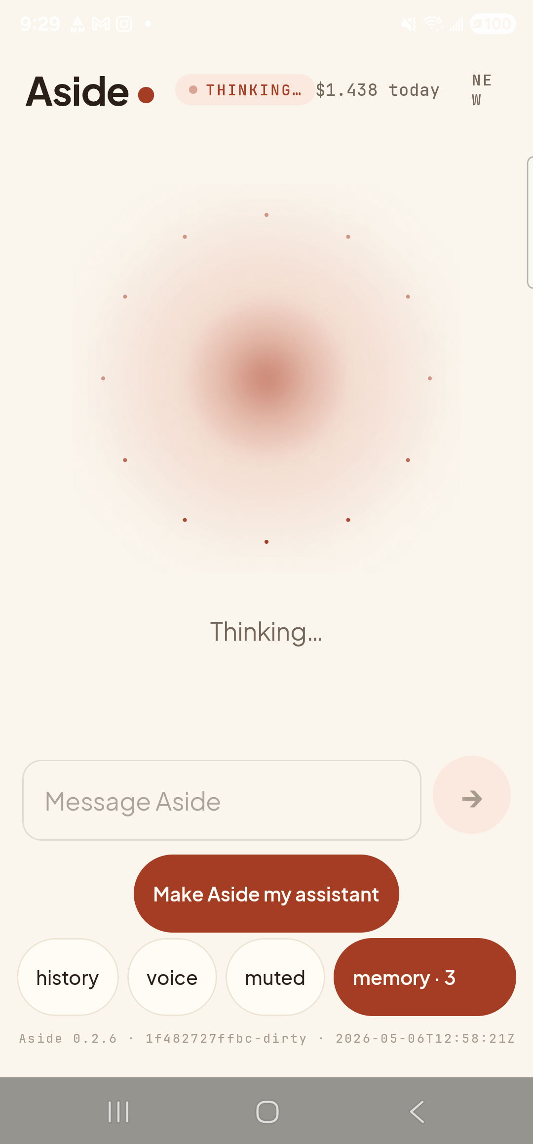 The Aside main screen now in the thinking state. The status pill at the top reads ‘● THINKING…’ and the cost counter still shows ‘$1.438 today’. The orb is the same warm shape, scattered with small dots. Beneath the orb a single line reads ‘Thinking…’. Below that the text-input field shows the placeholder ‘Message Aside’ with a clay send arrow on its right. The bottom pill row reads history, voice, muted, memory · 3.