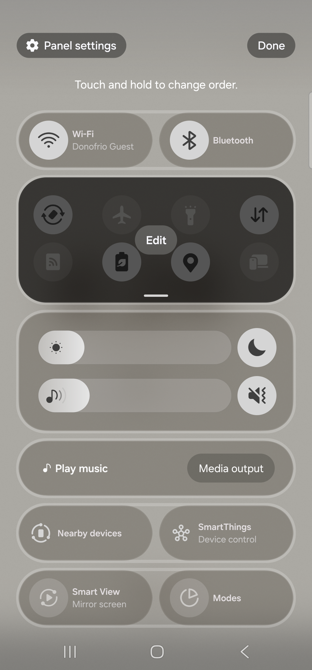 The Samsung One UI Quick Settings tray in edit mode. The header now shows ‘Panel settings’ at the top-left and a ‘Done’ pill button at the top-right, with caption ‘Touch and hold to change order.’ The first row of the tray shows large Wi-Fi and Bluetooth tiles. Below that, a dark rounded panel highlights the second row of tiles (Auto rotate, Flight mode, Flashlight, Mobile data, Mobile Hotspot, Power saving, Location, Link to Windows) with a small ‘Edit’ chip floating in the center. Below the active tray, additional rows show brightness, media controls, ‘Play music / Media output’, ‘Nearby devices / SmartThings’, and ‘Smart View / Modes’. (Note: on this device Aside’s tile may not yet be in the available list until SystemUI’s cache is refreshed by a phone restart, per the Samsung One UI 6 quirk.)